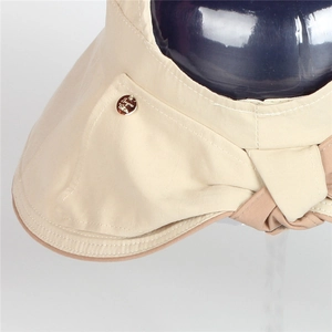 Detail of beige sun hat featuring gold metal brand tag and brown fabric edge binding