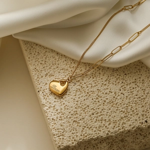 Collier avec pendentif cœur doré et chaîne trombone asymétrique sur satin blanc et pierre