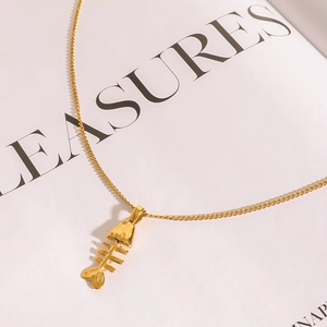 Collier élégant avec pendentif arête de poisson dorée sur un magazine au fini métallique