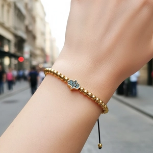 Golden bead bracelet with blue gem Hand of Fatima charm on a black adjustable cord