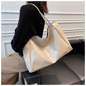 Detail of a large cream leather tote bag with side pleats shown on a model