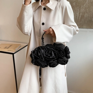 Detail of elegant black satin 3D rose evening bag with a beaded handle held by a model