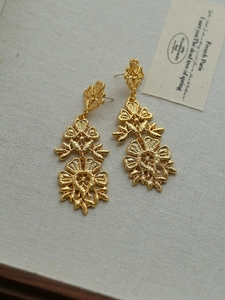 Macro shot of vintage gold hollow flower earrings on linen with French poetic card background