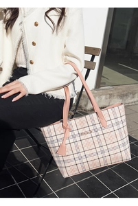 Detailed view of pink plaid tote bag with leather handles shown in an outdoor cafe setting