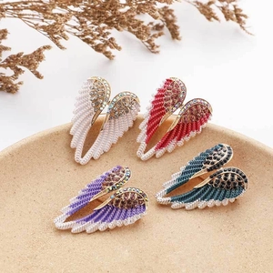 Detail showing angel wing brooches in four colors set on a beige textured jewelry tray
