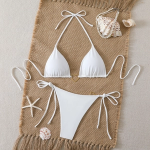 Flat lay of a white triangle bikini set with golden heart rings and beach accessories