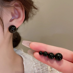 Detail showing four sizes of polished black round stud earrings worn and held by hand
