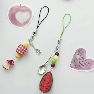 Handmade phone charms featuring miniature fruit, spoon and fork charms on white background