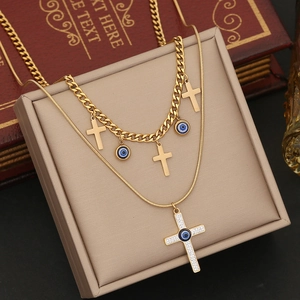 Double-layered gold cross and evil eye pendant necklace on a beige jewelry box