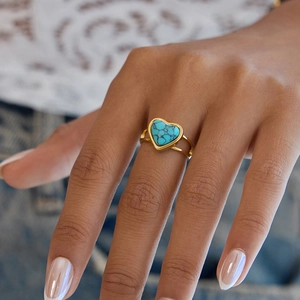Bague en acier doré avec pierre de turquoise en forme de cœur portée par un mannequin