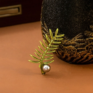 Detail shot of golden branch brooch with green leaves and a delicate white pearl accent
