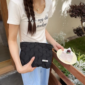 Close-up of black quilted handheld cosmetic bag with textured finish and brand label