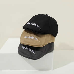 Detail of embroidered Say Hello text on cotton baby berets in black, khaki, and dark grey