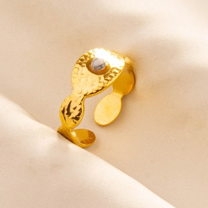 Detail of hammered gold adjustable ring with central white oval stone on soft fabric