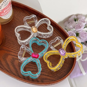 Three heart-shaped hair claws in white blue and yellow frames on a wooden tray