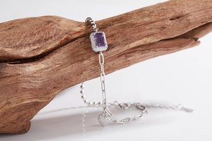 Detailed macro shot of silver chain bracelet with purple gem and heart charm on wood