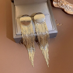 Detailed close-up of golden tassel earrings with brushed metal studs on a jewelry box