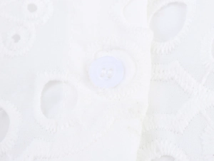 Detailed macro view of white embroidery hollow fabric with a classic four-hole round button