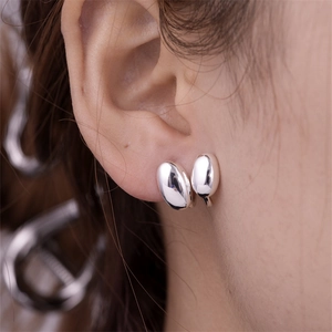 Macro side view of silver polished bean earrings with a mirror-like finish on the ear