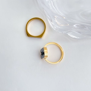 Detailed top view of gold rings with black enamel inlay and square crystal gemstone