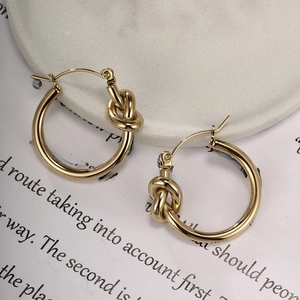 Close-up of golden geometric twisted knot hoop earrings on a white textured ceramic plate
