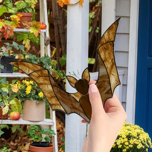 Close-up of a decorative bat pendant with amber textured wings held in a garden