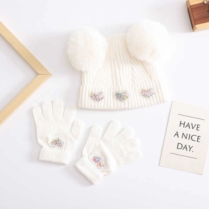 Detail of white knit baby hat with two fur pom-poms and matching sequin heart gloves