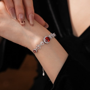 Detailed view of women's silver bracelet with oval red gemstone and zircon flowers