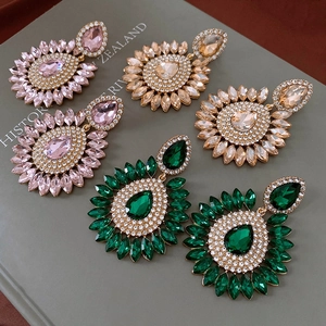 Gros plan de grandes boucles d'oreilles tournesol en forme de larme en rose, champagne et émeraude