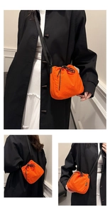 Orange nylon drawstring bucket bag with black thin strap worn on a black trench coat