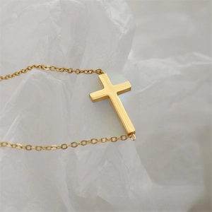 Macro shot of minimalist gold cross necklace pendant with polished steel link chain