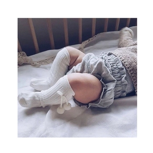Detail of baby knee-high socks with pom-poms and ribbed texture on white bedding