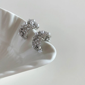 Close-up of silver C-shaped earrings with white pearls and sparkling zircons on a tray