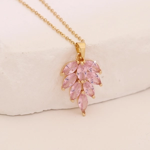 Macro detail of a golden leaf pendant necklace featuring marquise pink cubic zirconia stones