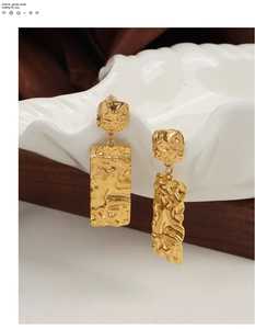 Detail of gold geometric earrings with hammered texture hanging on white ceramic plate