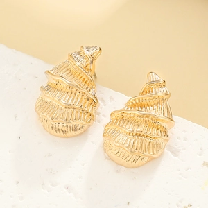 Macro shot of gold spiral shell earrings with textured finish on a white stone background