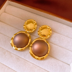 Close-up of vintage gold earrings with textured metal edges and matte brown center