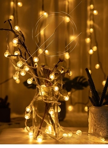 Detail of warm white LED globes wrapped around dry branches in a clear glass vase