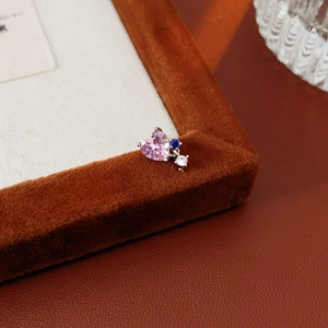 Macro shot of silver heart earring with pink zircon and blue gemstone on brown suede