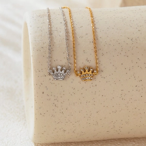 Detail of gold and silver crown necklaces with rhinestones on a beige ceramic cylinder