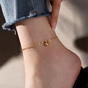 Detail view of a gold-plated titanium anklet with spherical bell charms on a model ankle