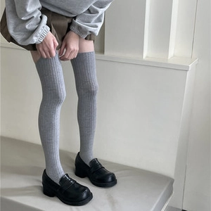 Detail of grey ribbed thigh high socks paired with black loafers and pleated skirt