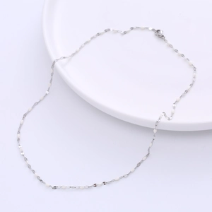 Detail of silver titanium chain necklace with white enamel beads on a white ceramic plate