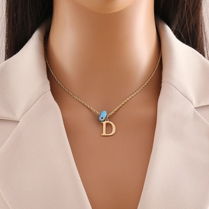 Close-up of model wearing gold chain necklace with letter D and blue eye bead pendant