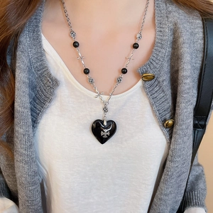 Detailed view of a gothic heart pendant necklace with cross relief on a grey sweater