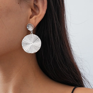 Close-up of model wearing textured silver circular geometric earrings with concentric patterns