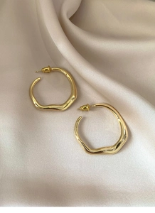 Detail shot of golden irregular hoop earrings on beige silk fabric with soft shadows