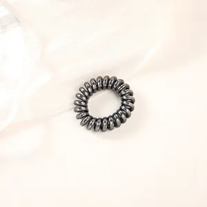 Detailed close-up of dark metallic spiral hair tie on elegant silk fabric background