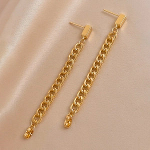 Close-up of golden long chain drop earrings resting on champagne silk fabric background
