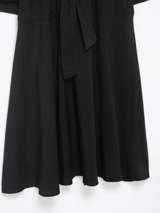 Detail of black trench midi dress featuring a woven waist tie and elegant flared skirt